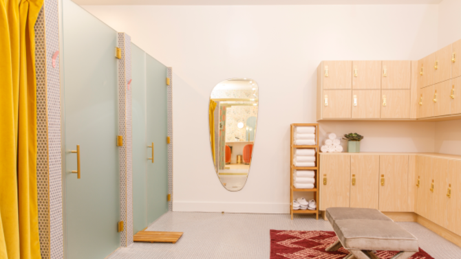 Large room with three showers on the left and lockers and towels on the right.