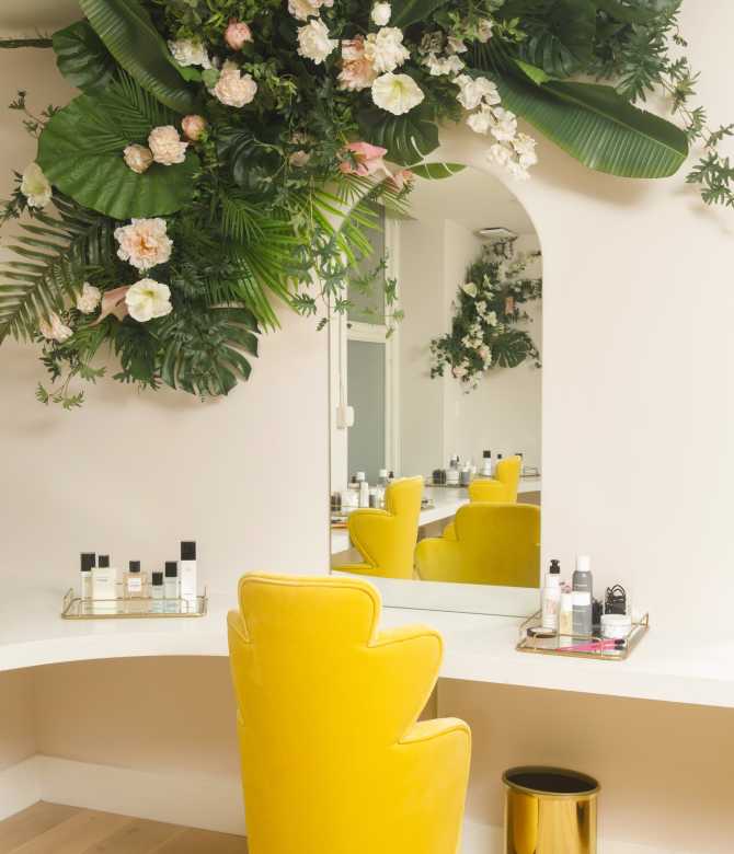 Long desk with mirror, bright yellow chair and jungle-like plants above.